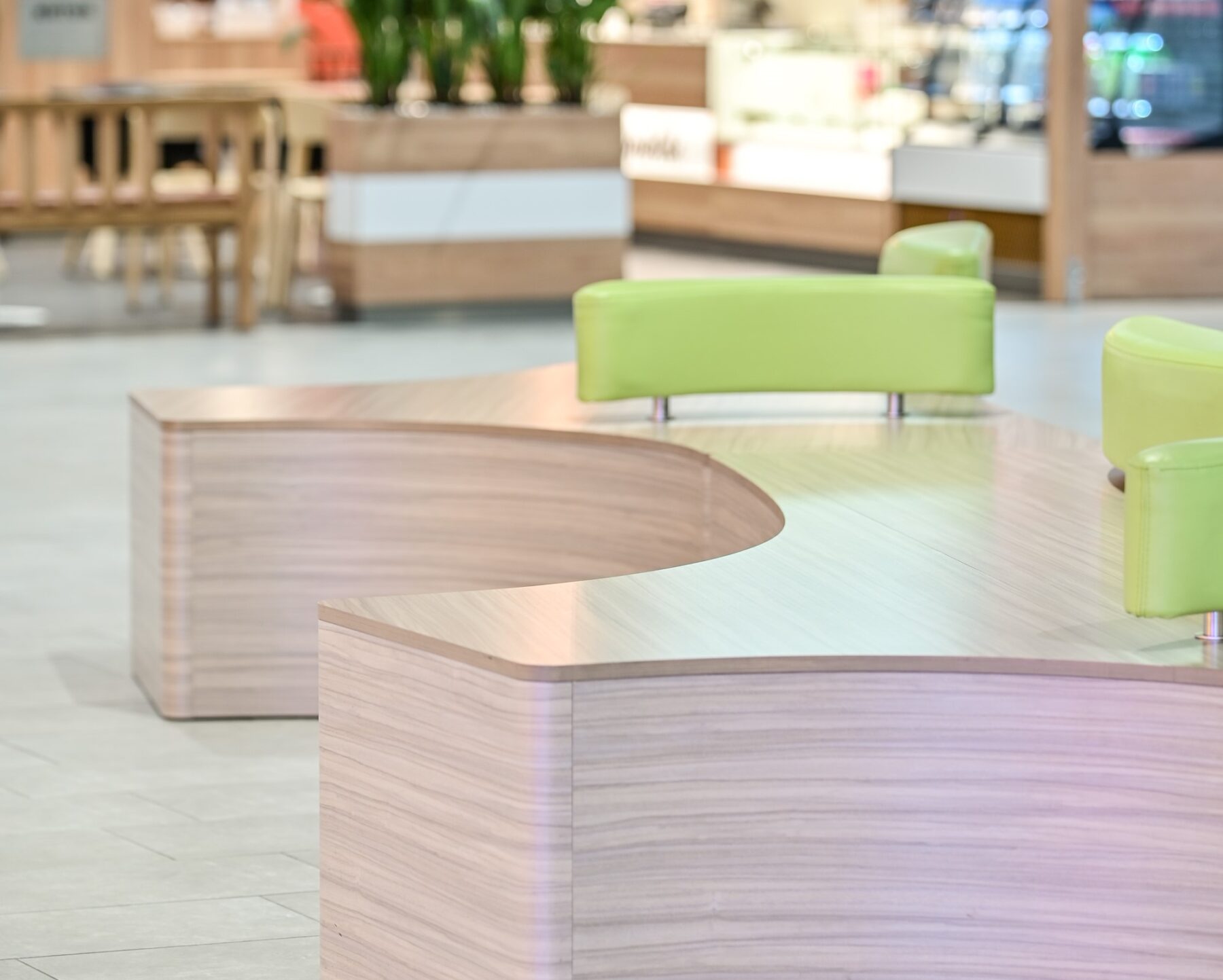 Ideapark Oulu C-aula julkitilan istuinkaluste, joka muodoltaan kolmisakarainen kaarevilla reunoilla. Vaalea puu laminaattipinta ja käsinojat kirkkaan vihreät. sisustussuunnittelu ja kalustemuotoilu Sisu interior.